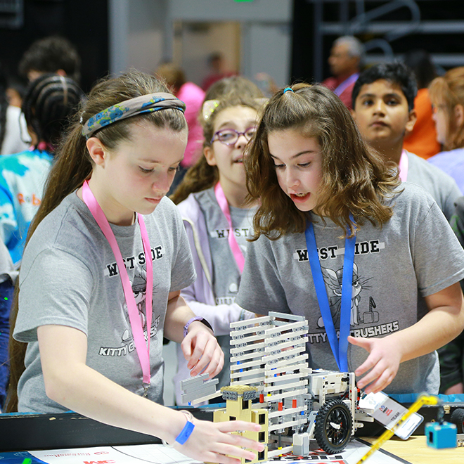 students working together on a robot at a first lego league table