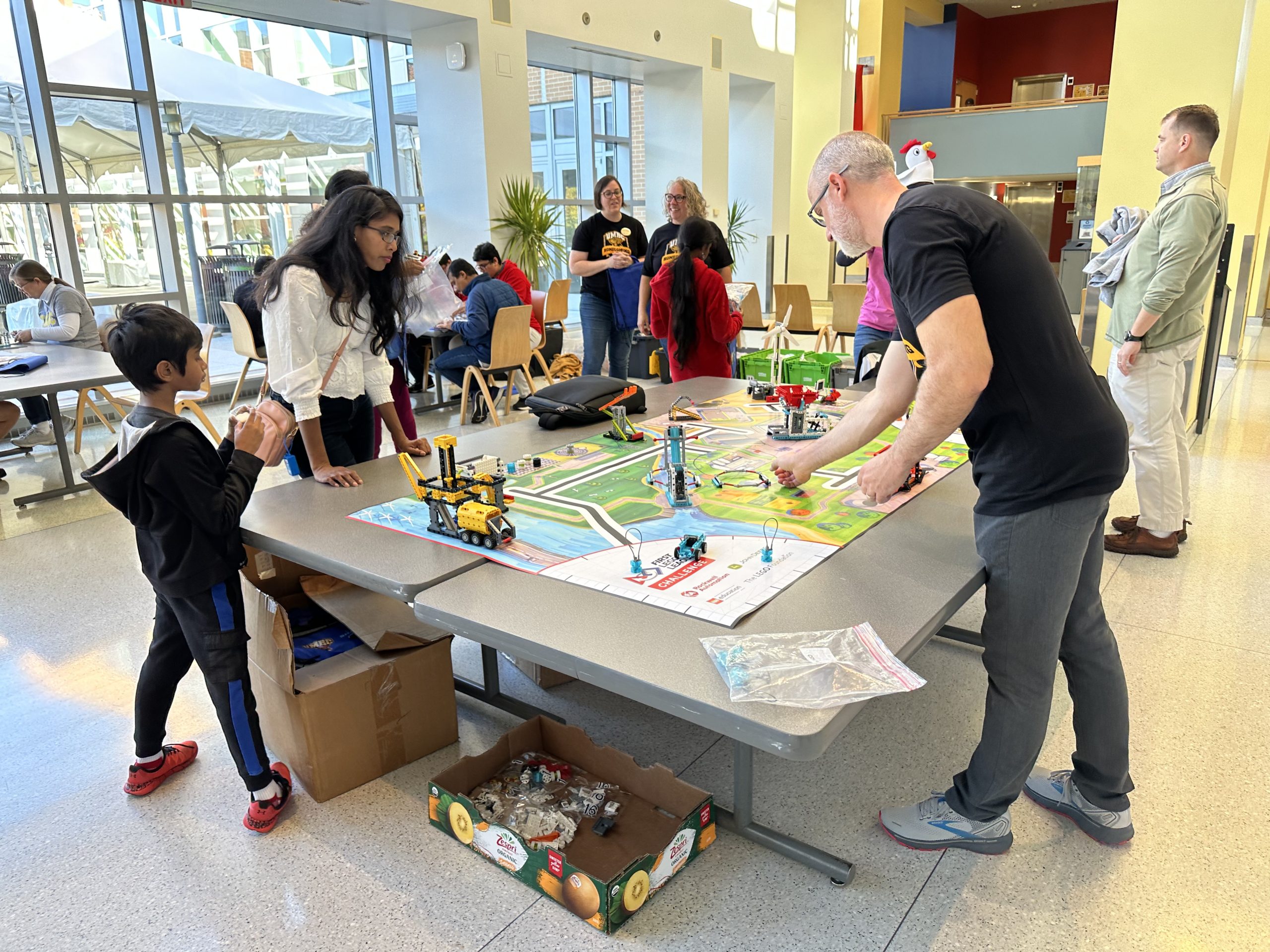 People gathered around a FIRST Lego League Challenge mat building models for competitions,